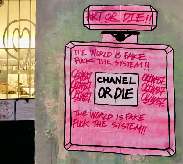 Graffito of a Chanel perfume bottle with the words The World Is Fake, Fuck the System written on it.